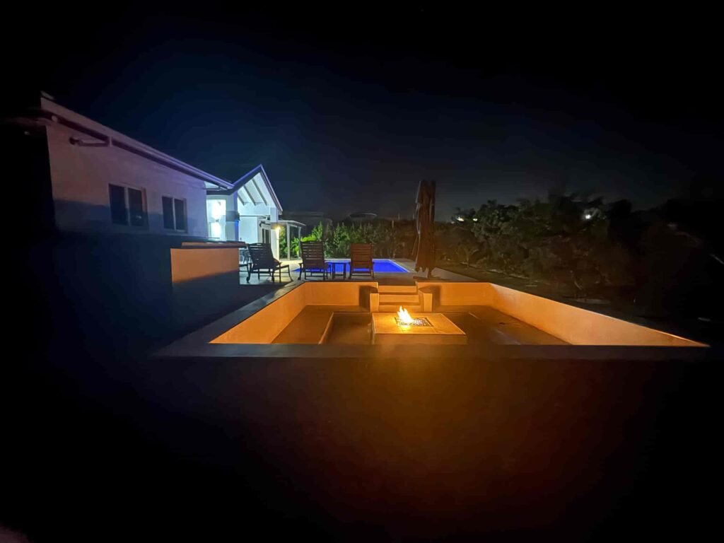 Blue Water Villa at night featuring a cozy outdoor fire pit, illuminated pool, and relaxing outdoor lounge in Grand Turk.