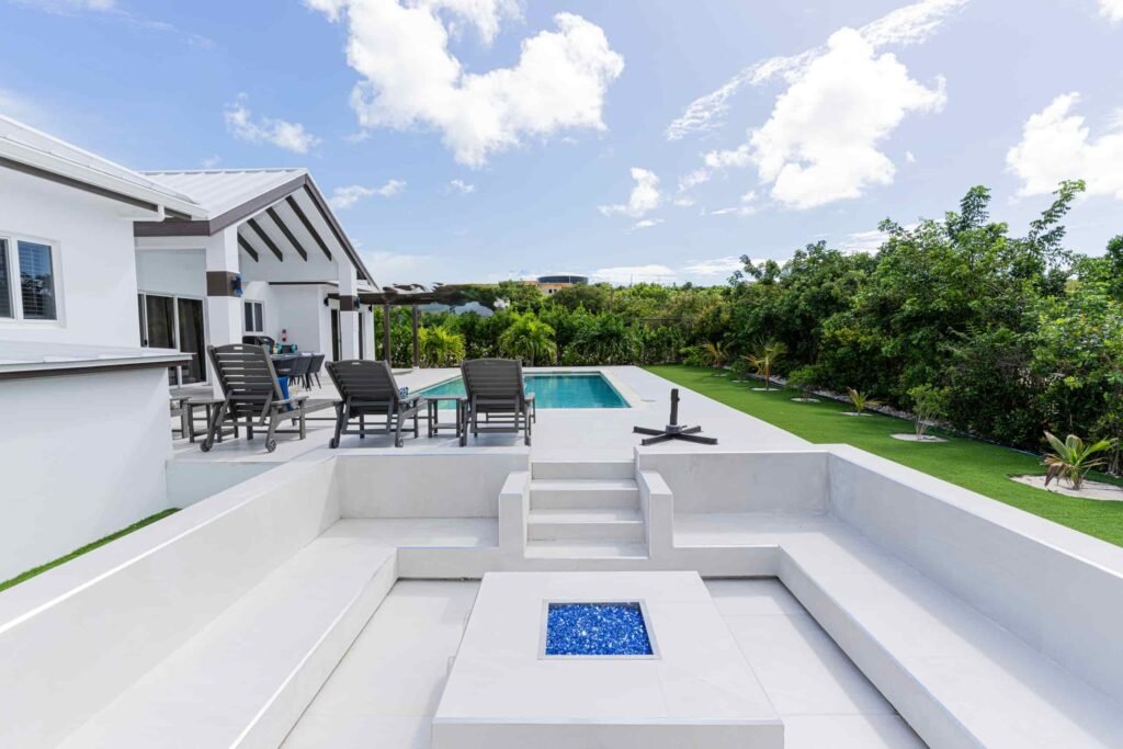 Outdoor seating area with a modern fire pit, pool, and tropical surroundings at Blue Water Villa.